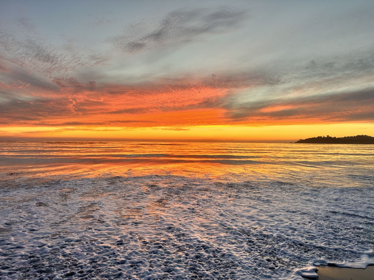 Sunset over the Pacific from Carmel Beach, the surf lit orange and gold.